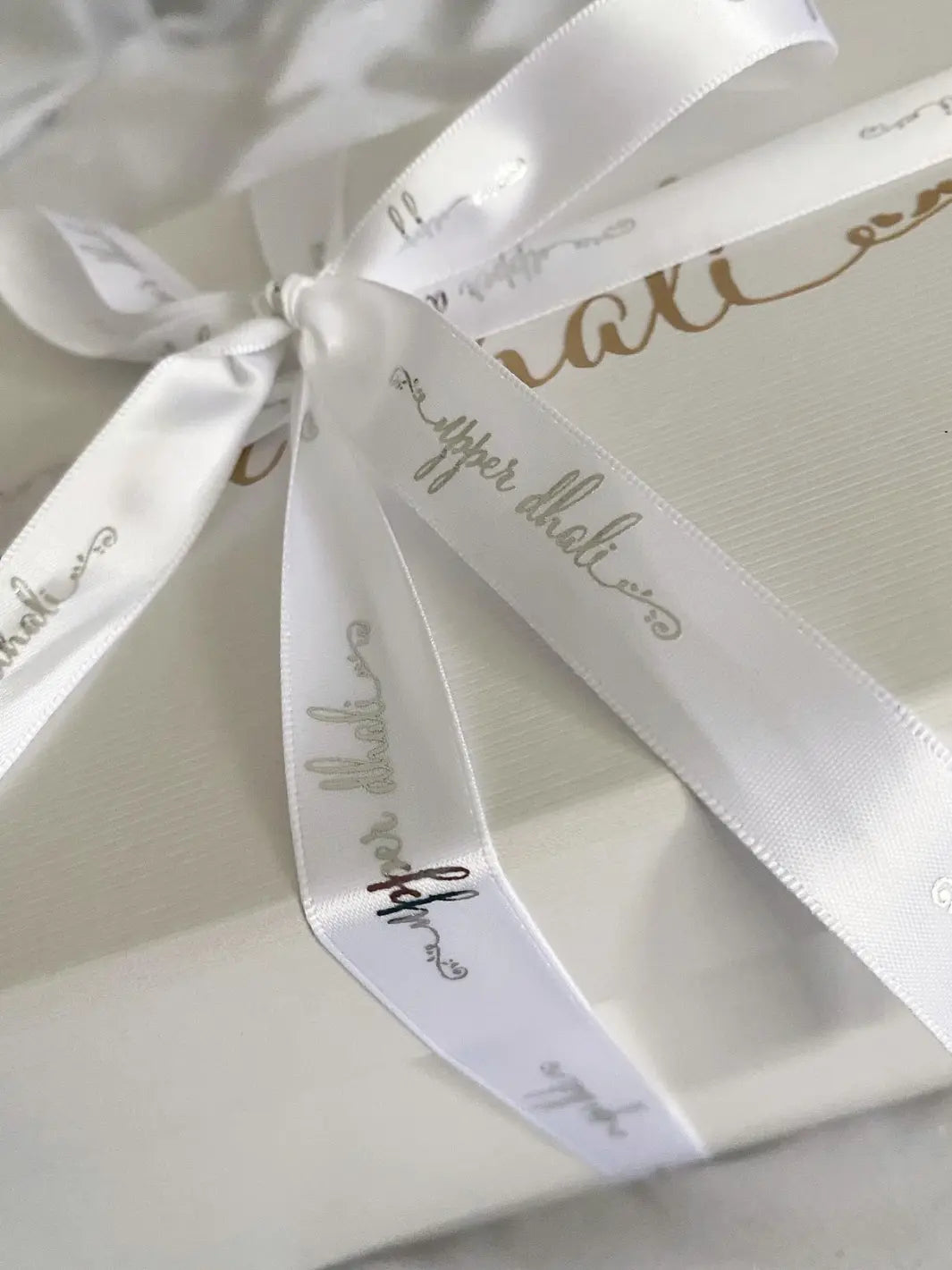 close up logo ribbon of white gifting box with gold logo & white satin ribbon for Upper Dhali handmade dolls