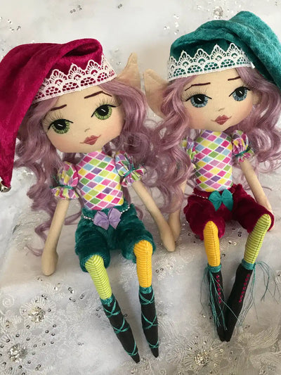 two handmade christmas elves sitting on a shelf. jewel coloured tones with velvet pants and hats, hand embroidered faces and cheeky grins