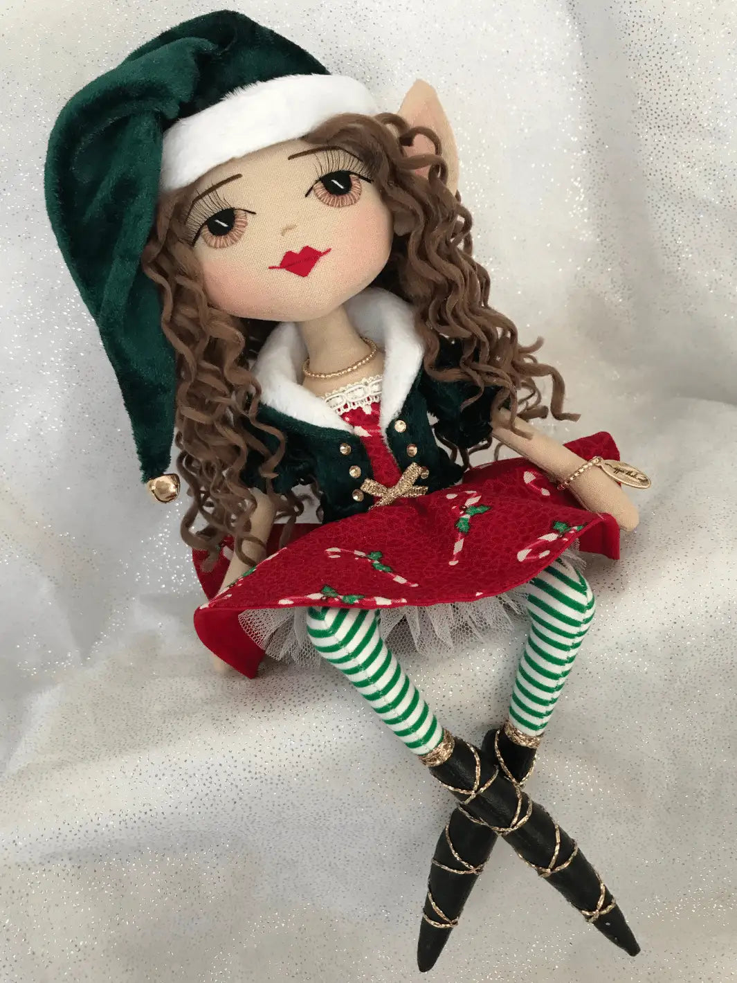 handmade christmas elf doll sitting on a shelf wearing a green velvet jacket with gold detail and a red circle skirt with candy cane design. She has hand embroidered hazel eyes and red lips.