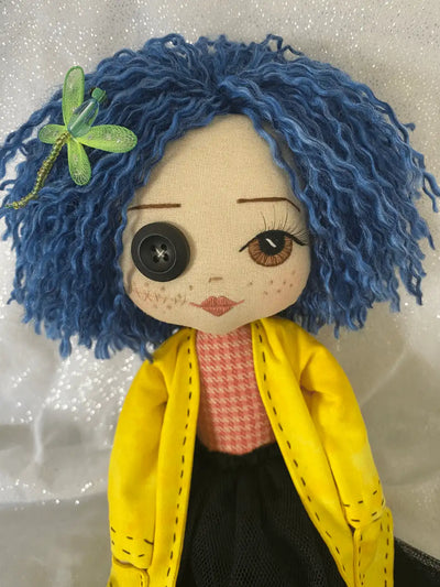 handmade doll with blue hair, hand embroidered face featuring one brown eye, one button eye, wearing a yellow jacket, red and orange shirt and a black tulle skirt
