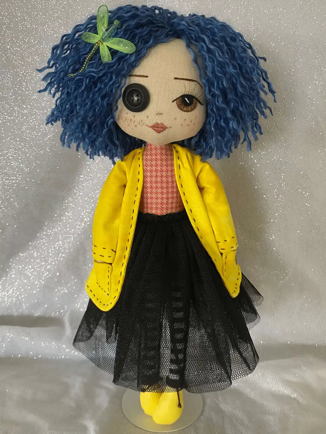 coraline handmade doll, blue hair, green dragonfly hairclip, one button eye, one hand embroidered brown eye, yellow jacket, red and orange shirt, black tulle skirt, black and white stripe tights and yellow boots