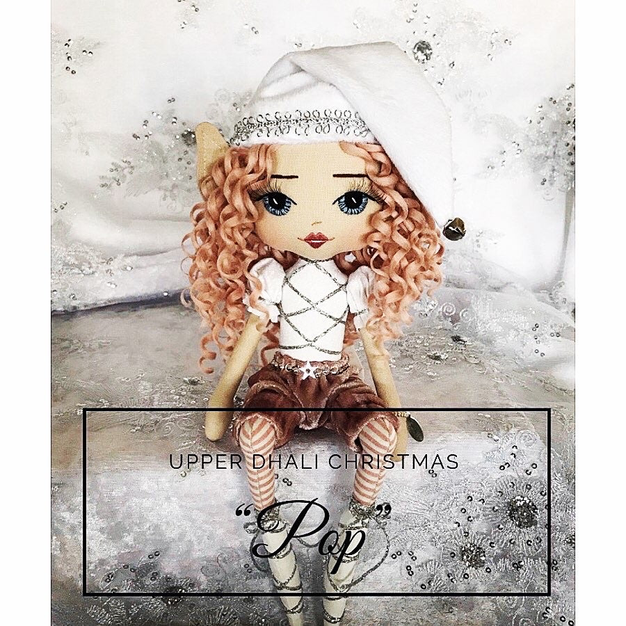 a white and pink christmas elf sitting on a shelf with white and silver backdrop