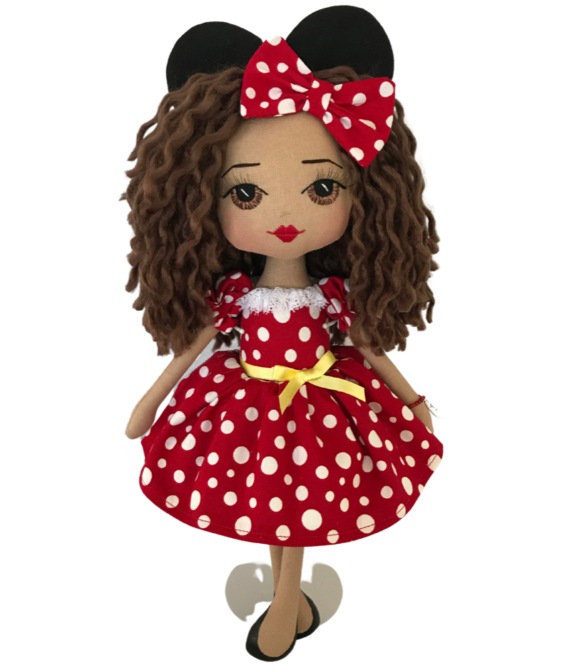 A handmade doll dressed in a red dress with white spots and a yellow ribbon around her waist. She also has a red with white spots bow in her hair and Minnie Mouse ears