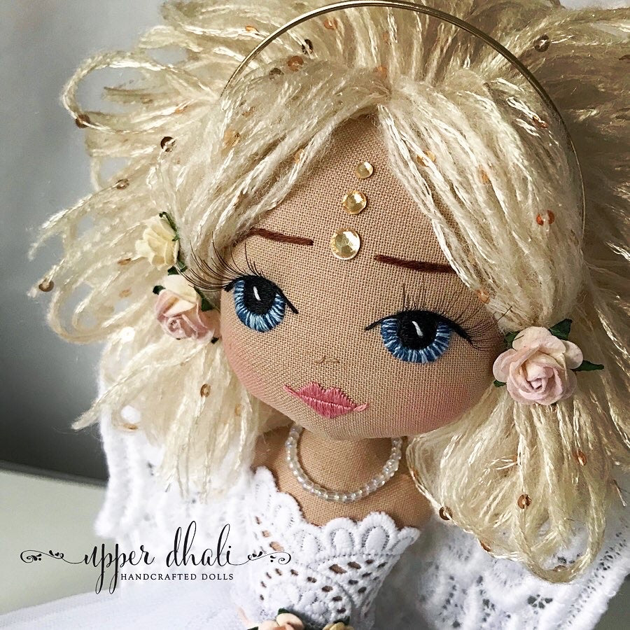 close up image of a handmade doll with blue eyes and blonde short hair with golden diamantes on her forehead