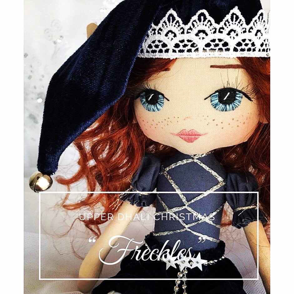 christmas elf wearing navy blue with red curly hair and blue hand embroidered eyes