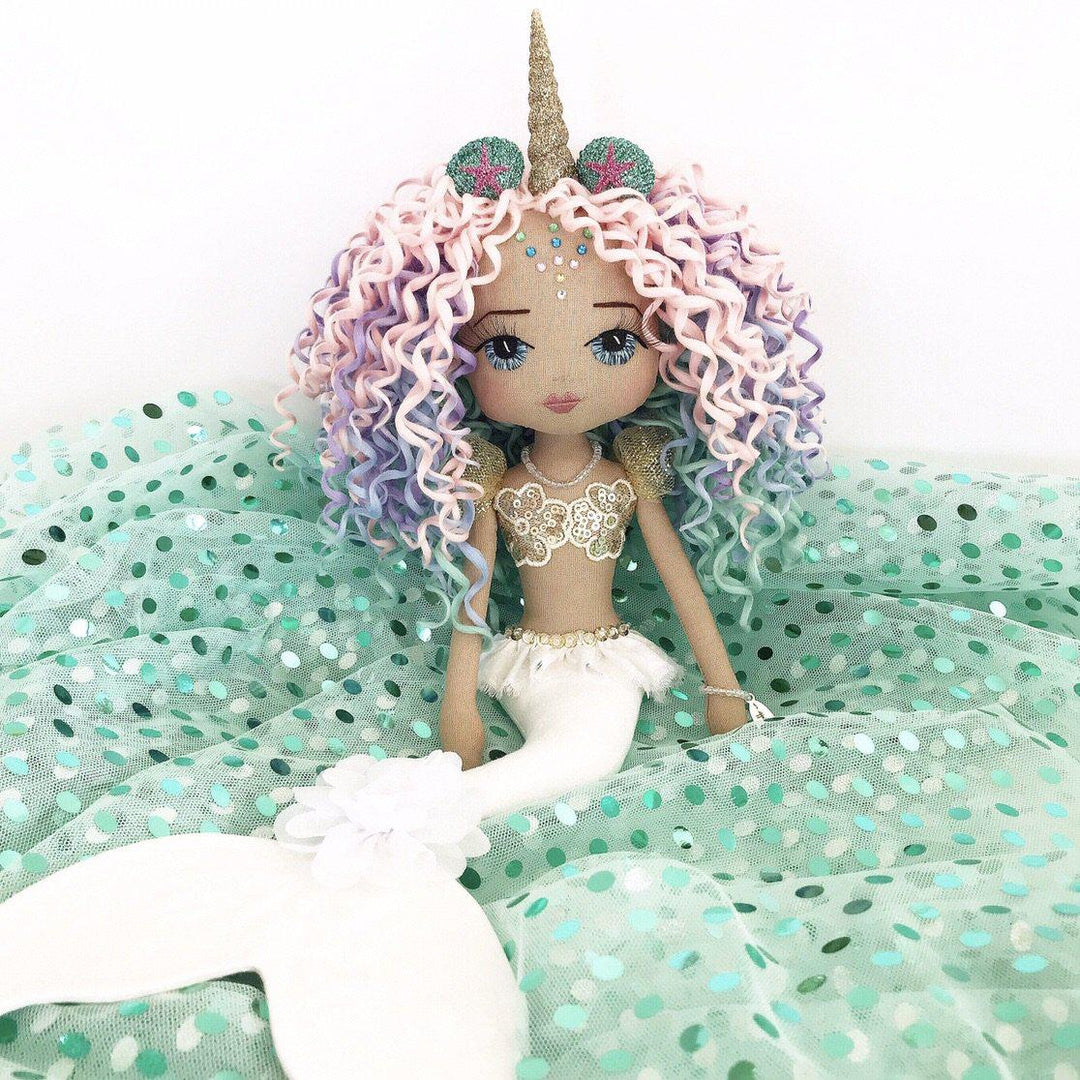 handmade doll with a white mermaid tail and a golden unicorn horn. Long curly hair in rainbow pastel colours, blue hand embroidered eyes, diamante forhead festive makeup and a golden mermaid top