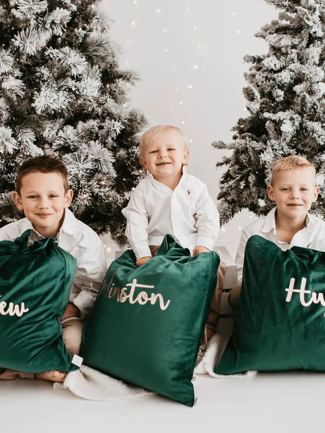green velvet christmas santa sacks with male children under white flocked christmas trees