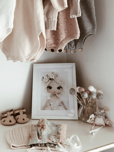 watercolour art print of a handmade doll displayed in a frame in a little girls nursery with baby clothing and shoes